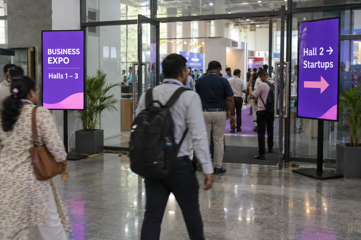 Visitors with lanyards passing purple wayfinding standees in an expo foyer